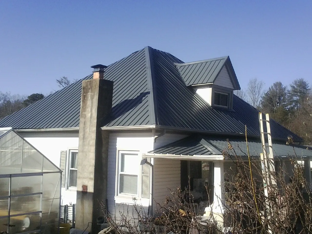 Dark blue standing seam metal roof on a white farmhouse with dormer — Slate & Tile Roof Repair by Roofing Brothers in Fairland