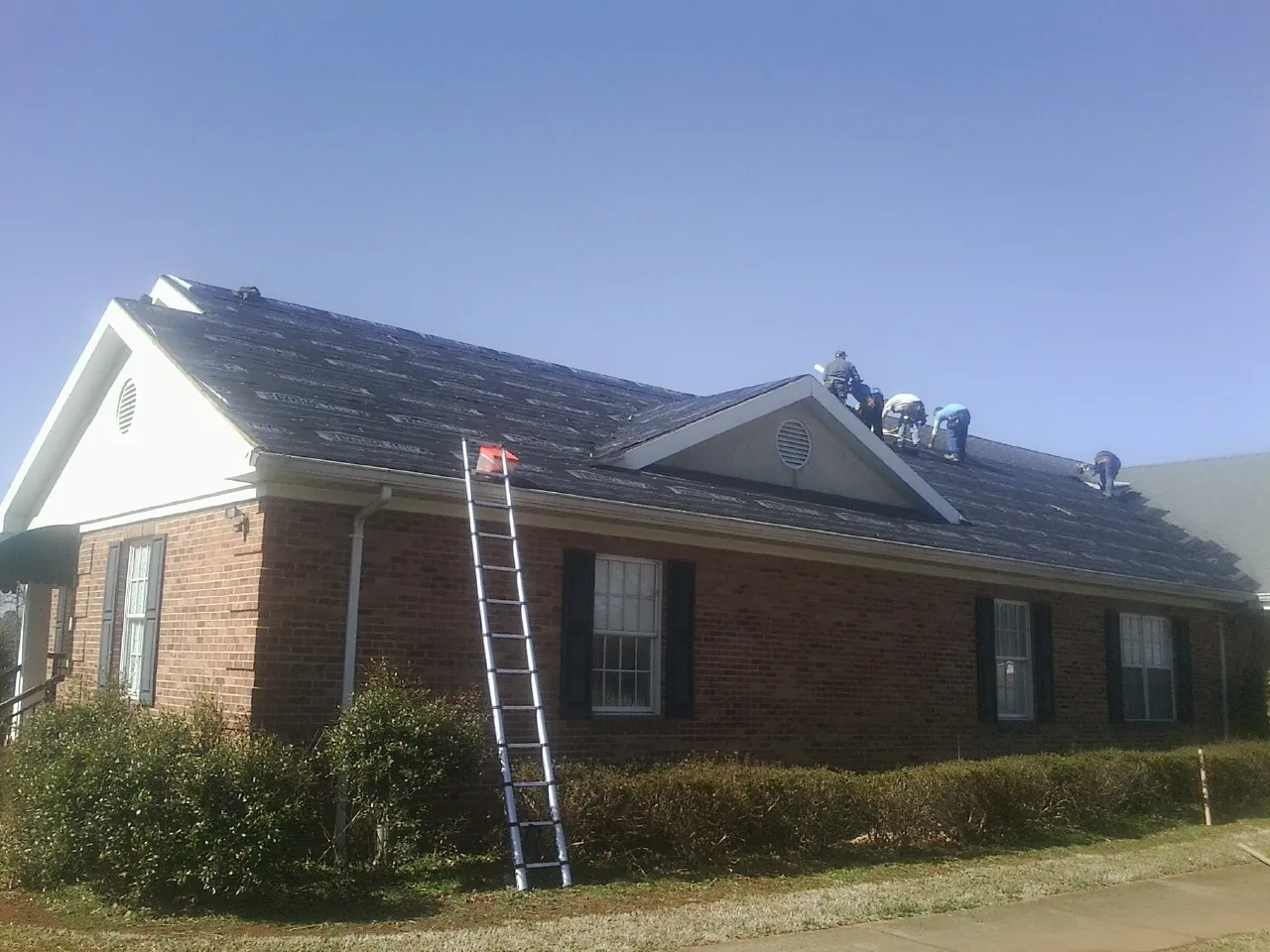 Crew tearing shingles off a brick ranch roof with a ladder set — Emergency Roof Repair work by our crew in Fairland