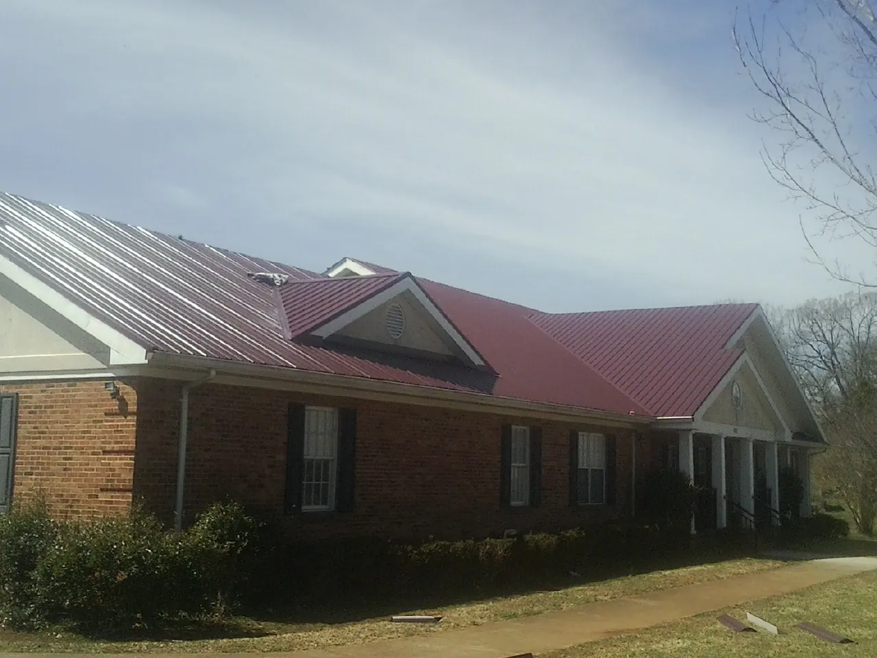 Red metal roof with gabled entries on a long brick building, from a Hail Damage Roof Repair job in Fairland