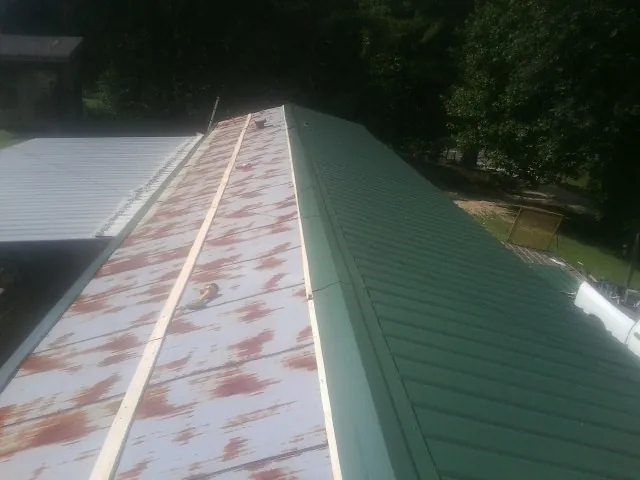 Old rusted panels beside newly installed green metal roofing — Wind Damage Roof Repair by Roofing Brothers in Fairland