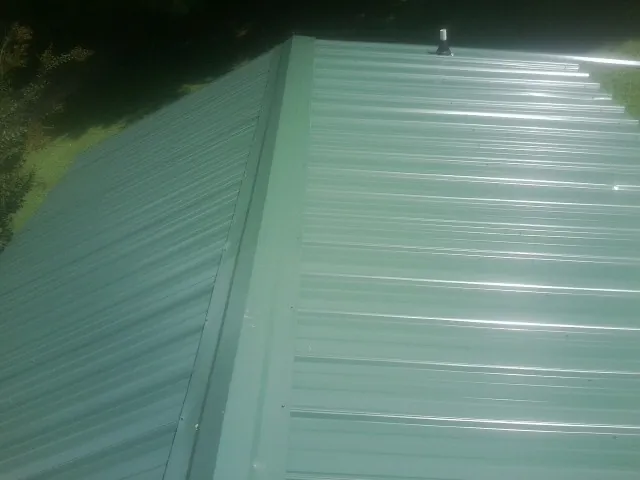 New green metal panels meeting at the ridge of a roof — Flat Roof Repair work by our crew in Fairland