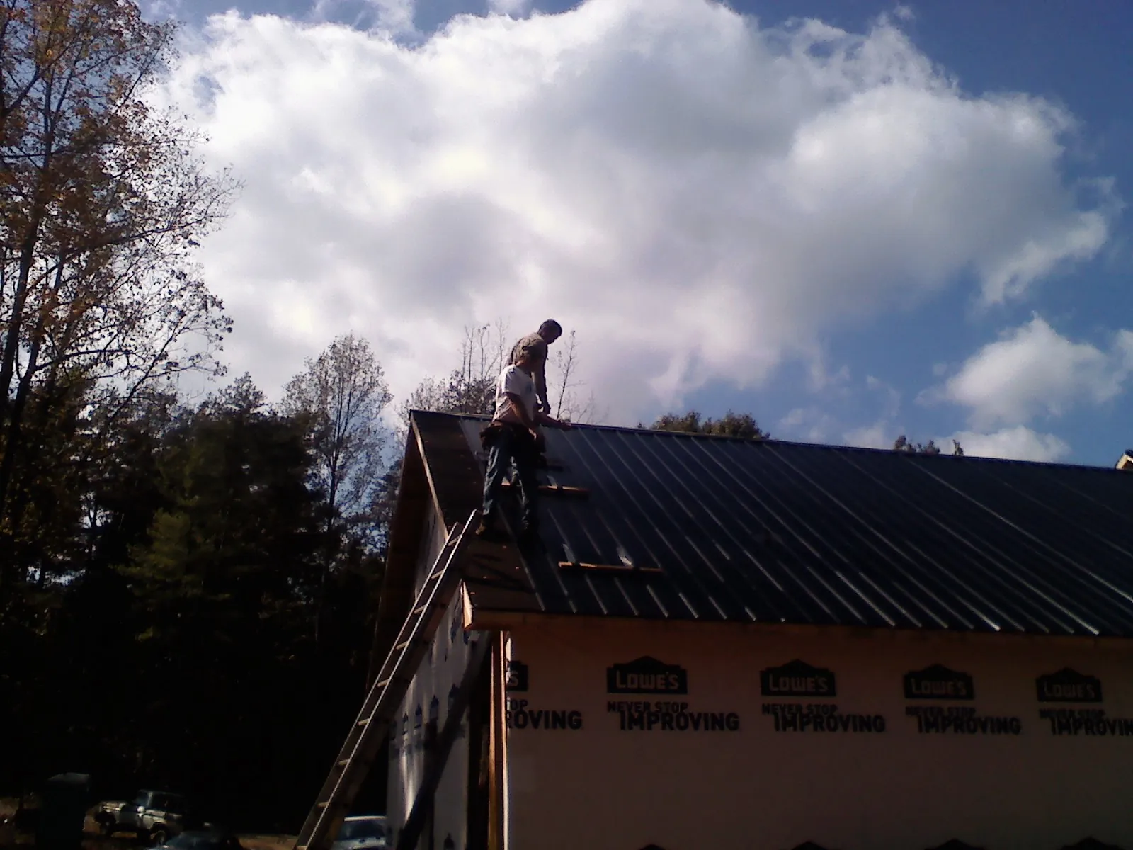 Roofer fastening dark metal panels high against a cloudy sky, from a Roof Inspection job in Fairland