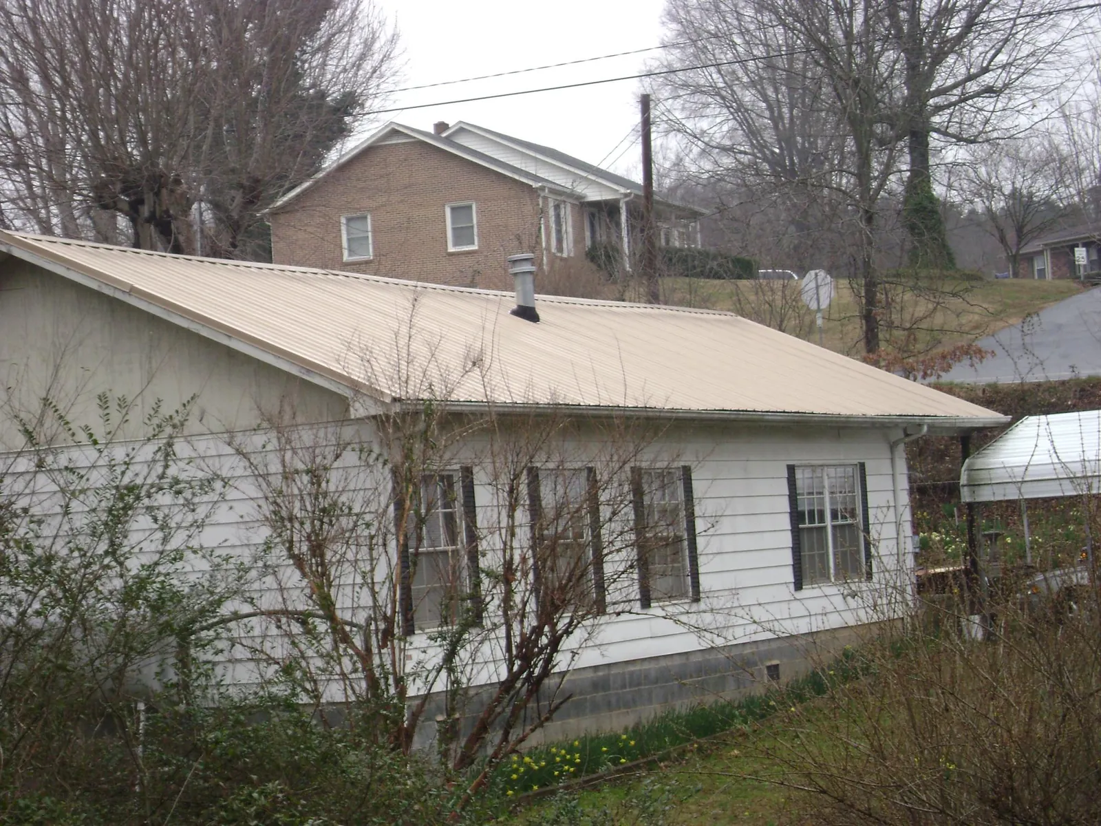 Tan metal roof on a white sided house set into a hillside — Commercial Roofing by Roofing Brothers in Fairland