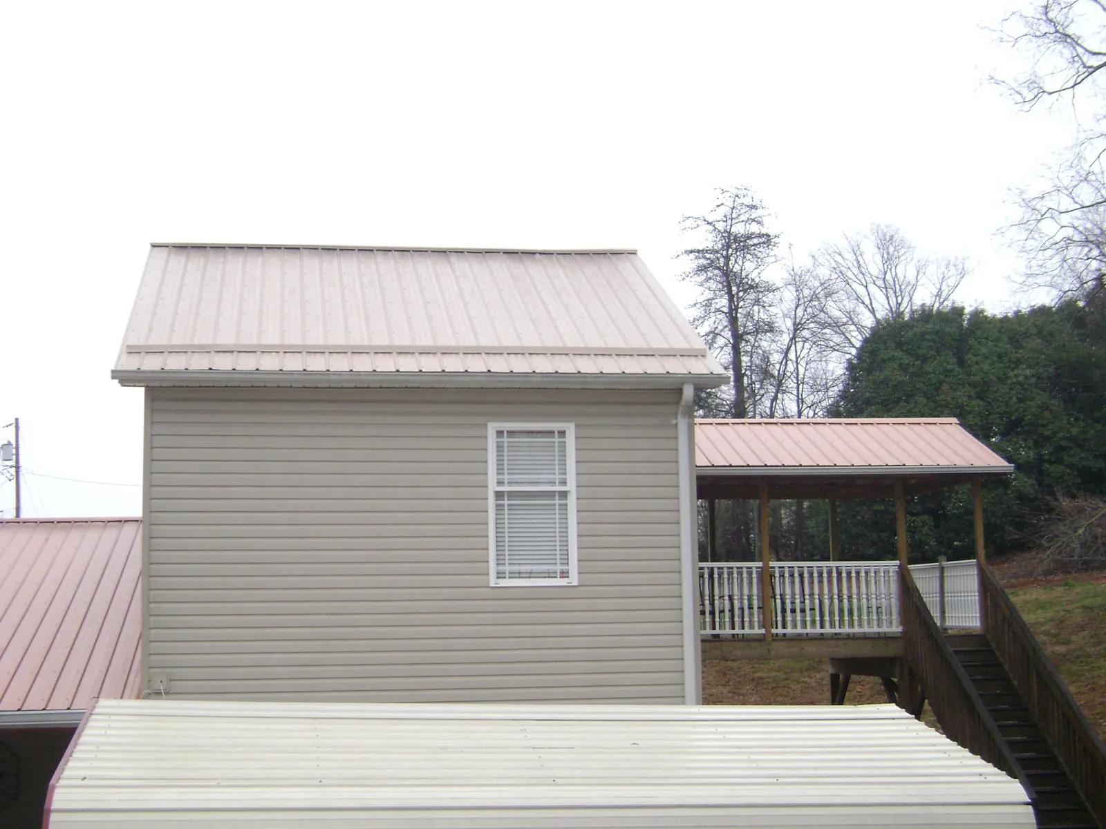 Tan metal roofs on a two story addition and attached porch, from a Roof Replacement job in Fairland